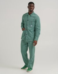 Veste en velours côtelé vert et pantalon assorti, avec un col, des poches avant et des rayures verticales texturées. Les accessoires comprennent des chaussures vertes.