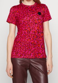 T-shirt rose à motif léopard avec un col rond et des manches courtes, présentant un petit accent noir sur la poitrine. Associé à un pantalon marron.