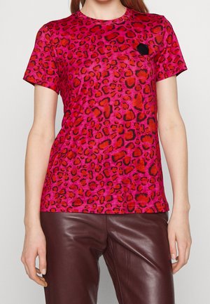 Roze T-shirt met luipaardprint, een ronde hals en korte mouwen, met een klein zwart detail op de borst. Gecombineerd met een bruine broek.