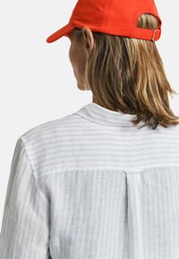 Wit en lichtblauw gestreept overhemd met een rugplooitje, gecombineerd met een helderrood pet met een gebogen rand en een verstelbare band.