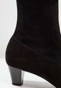 Bottine en daim noir avec talon carré bas et coutures apparentes sur une surface blanche.