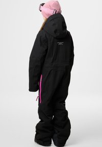 Zwarte sneeuwpak met een capuchon, voorzien van roze ritsaccenten en logo, textuur stof en een relaxte pasvorm. Draagt met een roze beanie.