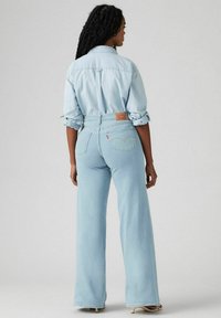 Lichtblauwe denim jeans met een hoge taille en brede pijpen, voorzien van een leren logo label op de achterkant en opgerolde mouwen van een bijpassend shirt.