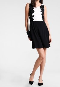 Robe sans manches en noir et blanc présentant un haut blanc uni et une jupe noire évasée, agrémentée de décorations florales noires sur les épaules.