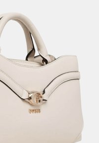 Borsa in finta pelle bianca con bordi neri, caratterizzata da un logo G dorato e il marchio GUESS sul davanti, progettata con bordi curvi e manici corti.
