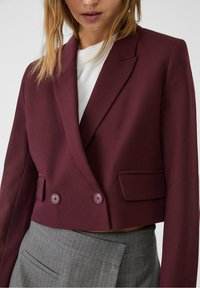 Bordeaux cropped blazer met dubbele knopen, scherpe revers en klepzakken; gecombineerd met een lichtgrijze pinstripe rok. Gladde stoftextuur.