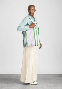 Drobės krepšys su vertikaliomis žaliomis, rožinėmis ir baltomis juostelėmis, pagamintas iš audinio. Turi viršutines rankenas ir minkštą, nesutrumpintą dizainą.