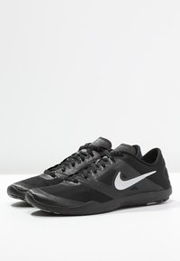 Black athletic shoes with a textured mesh upper, featuring a prominent silver Nike swoosh, flat laces, and a lightweight rubber outsole.