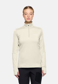 Lichtbeige, lange mouwen, ritsbovenstuk met hoge kraag, aansluitende pasvorm en zachte stof. Bevat een subtiele logo-detail op de borst.