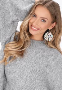 Runde Ohrringe mit aufwendigen floralen Mustern in zarten Farben, akzentuiert mit goldfarbenen Beschlägen, kombiniert mit einem gemütlichen grauen Pullover.