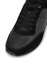 Čierna športová obuv s textúrovaným semišovým zvrškom a hladkými koženými akcentmi, s viazaním a gumovou podrážkou.
