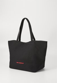 Sac fourre-tout noir en tissu texturé, doté de deux poignées robustes et d'un logo rouge "KARL LAGERFELD" sur le devant. Design minimaliste.