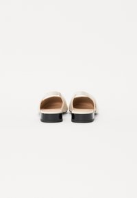 Chaussures blanches en cuir à bout ouvert avec un petit talon noir et un design épuré, comportant peu de détails et une texture lisse.