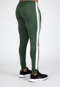 Groene sportbroek met witte zijkanten, voorzien van een elastische tailleband en een taperend model. Gemaakt in combinatie met zwarte sneakers met merkdetails.