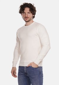 Maglione lungo beige chiaro a maniche lunghe realizzato in morbido tessuto a maglia, con scollatura rotonda e design aderente. Abbinato a jeans in denim blu.