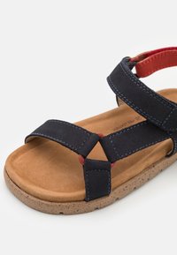Marineblå sandaler med to brede stropper, røde detaljer, korksåle og kontraststing. Har en blød fodseng og justerbare stropper.