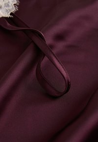 Material din satin burgund cu textură netedă, accent detaliat din dantelă și o legătură simplă și elegantă în formă de panglică.