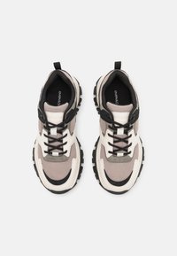 Chaussures de sport avec une tige en maille beige et des accents gris, des lacets noirs, une semelle blanche épaisse et une traction en caoutchouc noir.