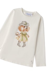 Langärmliges, cremefarbenes Hemd mit einem bedruckten Grafikdesign eines Puddels in einem gepunkteten Hut und Kleid, mit grünem Band und gepunkteten Stiefeln.