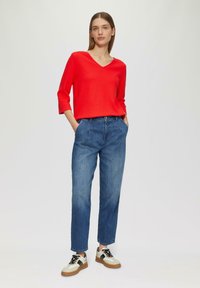 Maglietta rossa con scollatura a V e maniche a tre quarti abbinata a jeans denim blu a vestibilità comoda e sneakers multicolori con lacci neri e suola beige.