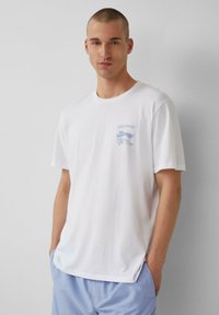 Weißes Baumwoll-T-Shirt mit kurzen Ärmeln, ausgestattet mit einem hellblauen Grafikdesign auf der linken Brust, lockere Passform und weichem Material.