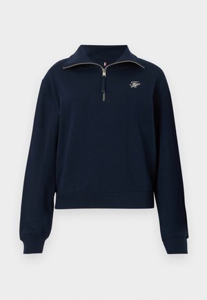 Marineblauwe lange mouwen pullover met half-rits kraag en klein wit geborduurd logo op de linkerkant van de borst.