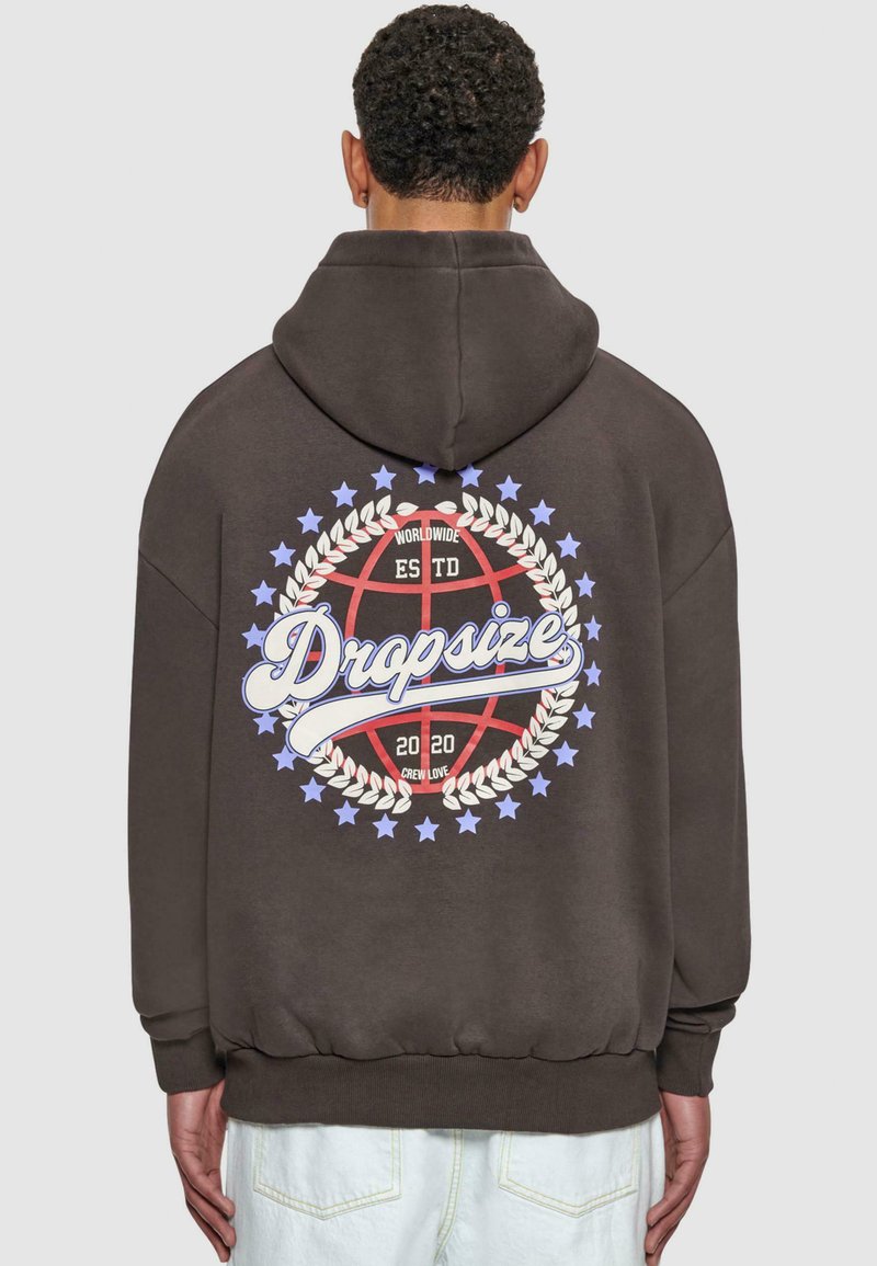 Brauner Kapuzenpullover mit Kapuze, der auf der Rückseite ein großes Grafikdesign zeigt: einen Basketball, umgeben von einem Lorbeerkranz, Text und Sternen.