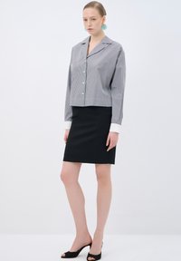 Grå och vit randig kortärmad blus med långa ärmar och en urklippt krage, tillsammans med en svart knälång kjol och svarta öppna klackskor.