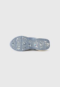 Semelle d’une chaussure de sport grise et blanche avec un motif géométrique et un petit logo au centre sur un fond clair uni.
