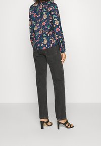 Blouse florale marine à manches longues, avec des fleurs et des feuilles multicolores. Associée à un jean droit gris foncé et des sandales à talons noires.