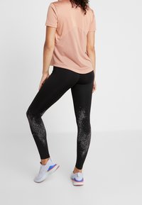 Rosa kortärmad skjorta med mesh-detaljer, svarta leggings med ett prickmönster, och grå sportskor med färgglada sulor.