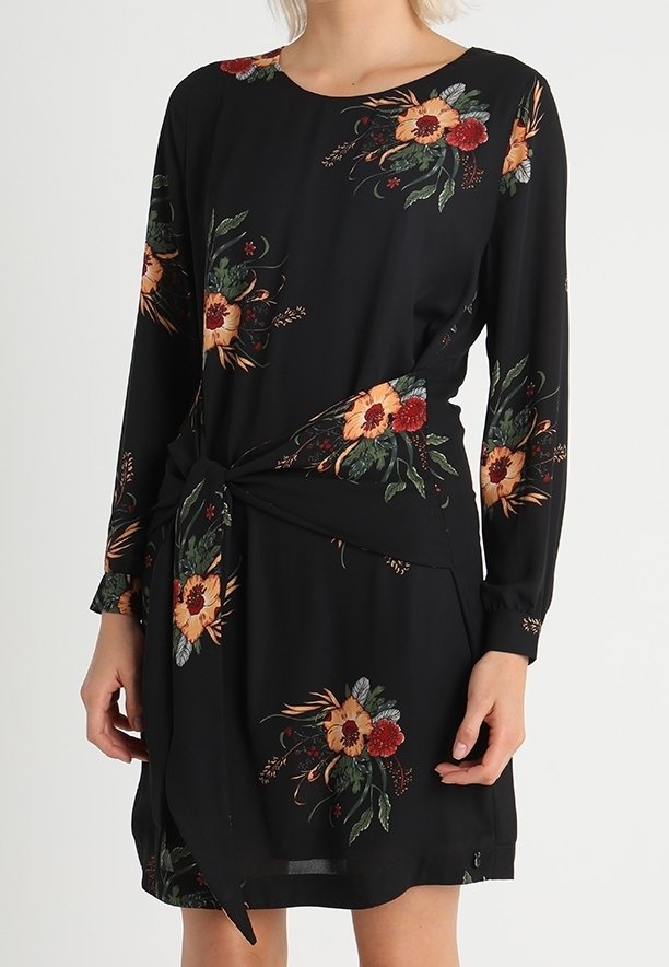 Vestido negro de manga larga, con patrones florales en rojo, naranja y verde. Detalle de cintura atada, tejido suave, longitud por encima de la rodilla.
