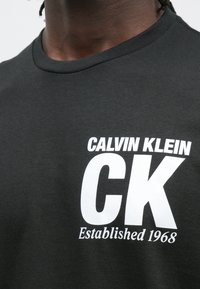 Czarna bawełniana koszulka z białym logo i napisem "CALVIN KLEIN CK Established 1968." Okrągły dekolt, krótkie rękawy i gładka faktura.