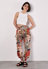 Pantalones cargo rojos y estampados con diseños florales, banda elástica en la cintura y puños en los tobillos, combinados con una blusa sin mangas blanca y sandalias negras.