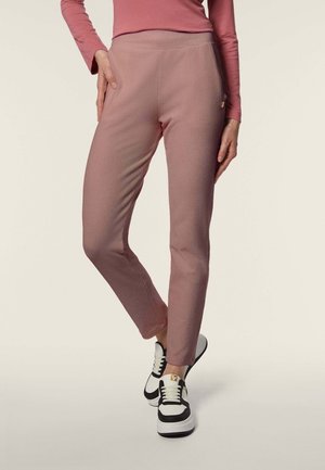 Pantaloni a vita alta rosa con una texture liscia e una vestibilità slim, abbinati a sneakers bianco e nere con un accento dorato.