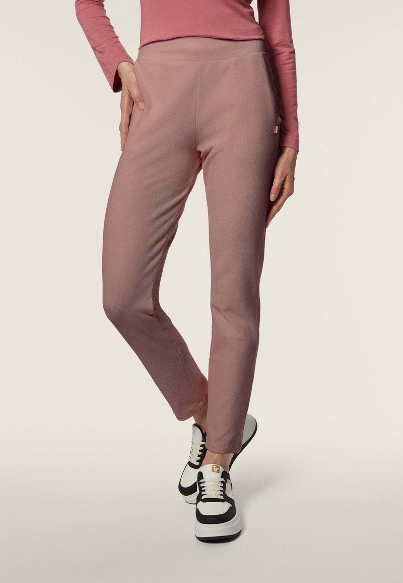 Pantaloni a vita alta rosa con una texture liscia e una vestibilità slim, abbinati a sneakers bianco e nere con un accento dorato.