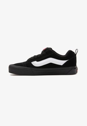 Sneaker in suede nero con dettagli bianchi, suola in gomma e chiusura con lacci. Presenta un colletto imbottito e un piccolo tab sul tallone per facilitare la calzata.