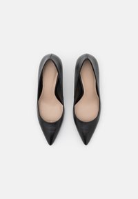 Black leather high-heeled shoes with a pointed toe, smooth texture, and a beige insole. Minimalistic design without visible hardware or accents.