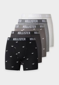 Пет чифта мъжки боксерки на Hollister в черно, тъмносиво, средносиво, светлосиво и бяло, подредени на стълбичка.