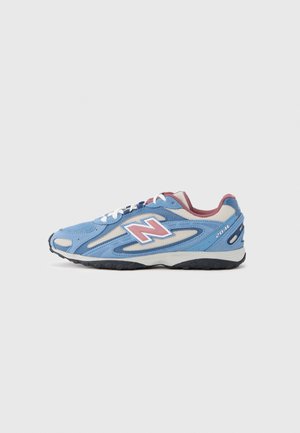 Niebiesko-beżowy but do biegania New Balance z różowymi i białymi akcentami oraz białymi sznurowadłami, pokazany z boku na jednolitym tle.