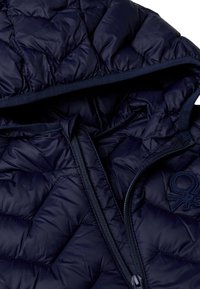 Giacca imbottita blu navy con cappuccio, dotata di chiusura a zip e dettaglio del logo ricamato. Materiale liscio e lucido con una texture morbida.