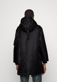 Cappotto nero con cappuccio e una texture liscia e tessuta. Presenta un cappuccio aderente, maniche lunghe e una cinghia regolabile sul retro per una migliore vestibilità.