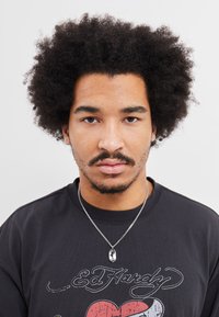 T-shirt preta com um design gráfico apresentando o texto "Ed Hardy" e um coração vermelho. Colar metálico com um pendente oval numa corrente prateada.