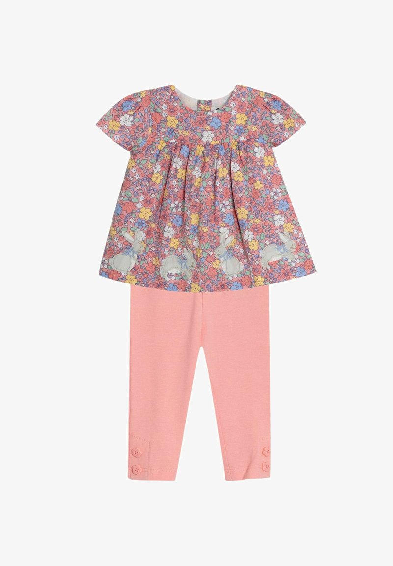 Bluse mit Blumenmuster und kurzen Ärmeln, die mit Hasen verziert ist, kombiniert mit einfarbigen pinken Leggings mit Knopfakzenten an den Knöcheln.