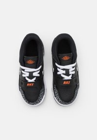 Black Nike sneakers with a textured pattern on the sole, white laces, and an orange logo on the strap. Rounded toe and padded collar.