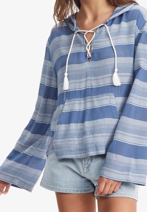 Personne portant un haut à capuche rayé bleu et blanc à manches longues larges et un short en jean bleu clair.