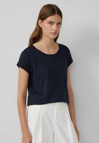 Granatowa koszulka z krótkim rękawem, okrągłym dekoltem, wykonana z miękkiego materiału; zestawiona z białymi spodniami o wysokim stanie. Minimalistyczny design.