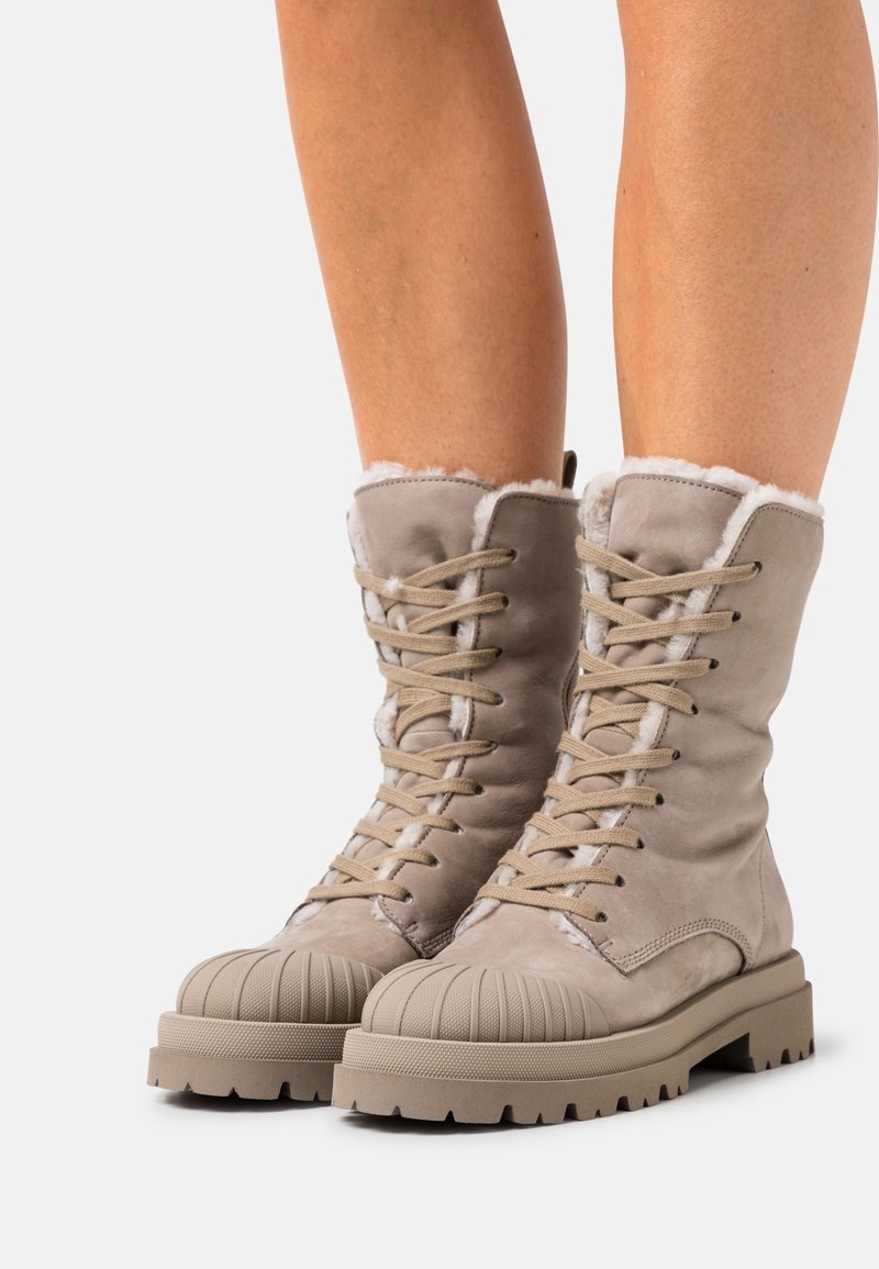 Beige veterschoenen tot de enkel met een zachte suede bovenkant, furry voering, ribbelige rubberen neus en een chunky, gestructureerde zool.