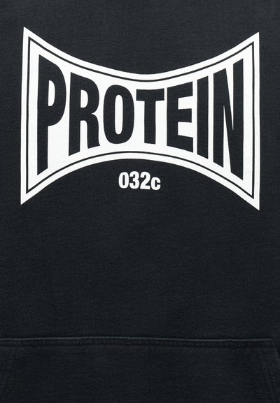 Čierna tkanina s bielym tučným textom „PROTEIN“ v natiahnutom obdĺžnikovom tvare a menším textom „032c“ pod slovom.
