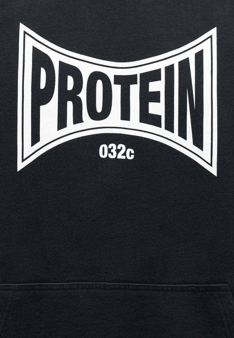 Zwarte stof met witte, vetgedrukte tekst "PROTEIN" in een uitgerekte rechthoekige vorm en kleinere tekst "032c" onder het woord.